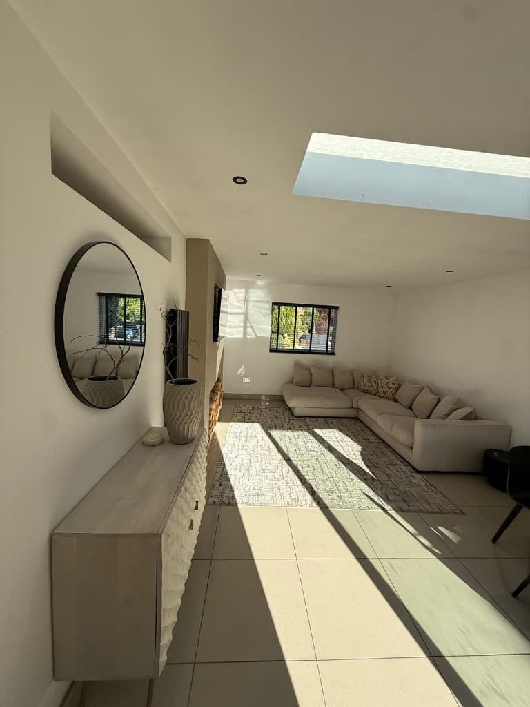 Bright living room with skylight, cream sectional sofa, geometric sideboard, and tiled floors after deep cleaning