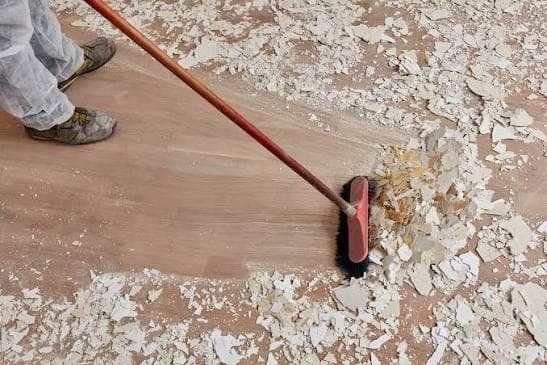Cleaner sweeping plaster dust and construction debris from a wooden floor during post-build cleaning