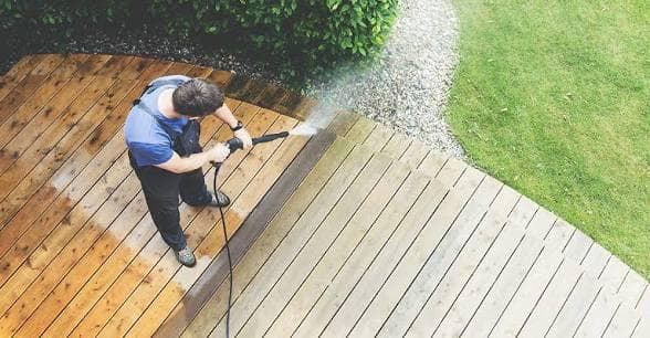 Professional jet washing a weathered wooden deck, showing a clear before-and-after restoration from greyed timber to clean natural wood