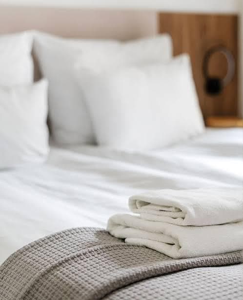 Professionally made bed with crisp white linens and freshly laundered towels folded on a grey throw at the foot of the bed