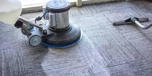 Professional floor scrubbing machine deep-cleaning grey patterned carpet tiles in a commercial office space