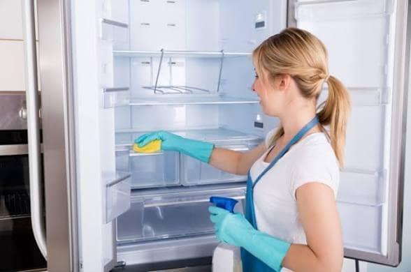 Professional cleaner wearing blue gloves wiping fridge shelves with a sponge during a tenancy changeover kitchen clean