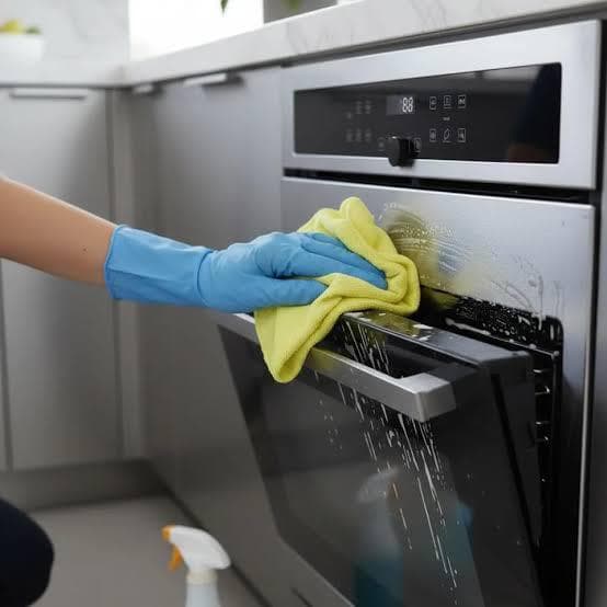 Yellow microfibre cloth wiping soapy foam from an oven door glass during a professional appliance clean
