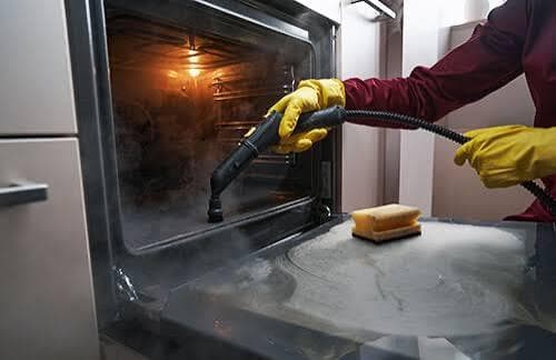Steam cleaning the interior of a built-in oven during a professional deep clean, with white vapour lifting grease and residue