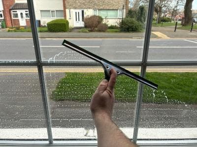 Squeegee clearing soapy water from an interior window pane, with a residential street visible through the glass